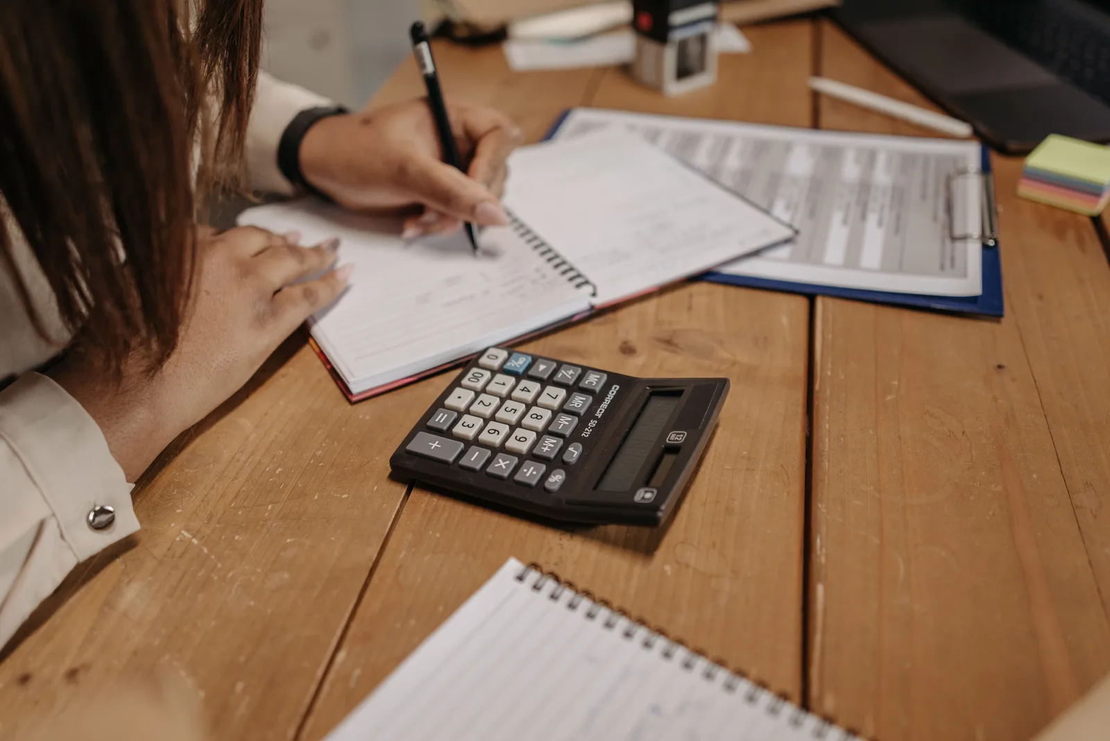 Woman writing notes with a calculator on a wooden desk, focusing on work and accounting. Bookkeeping firms: the parts worth your attention